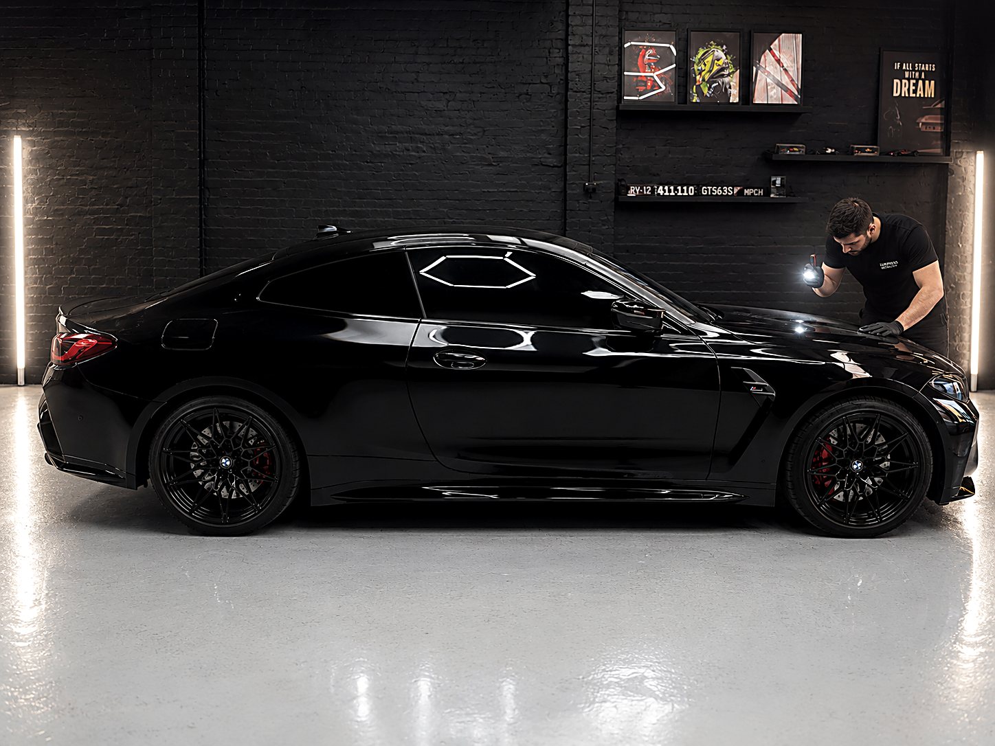 Luxpress detailer inspecting a black BMW M2 under studio inspection lighting